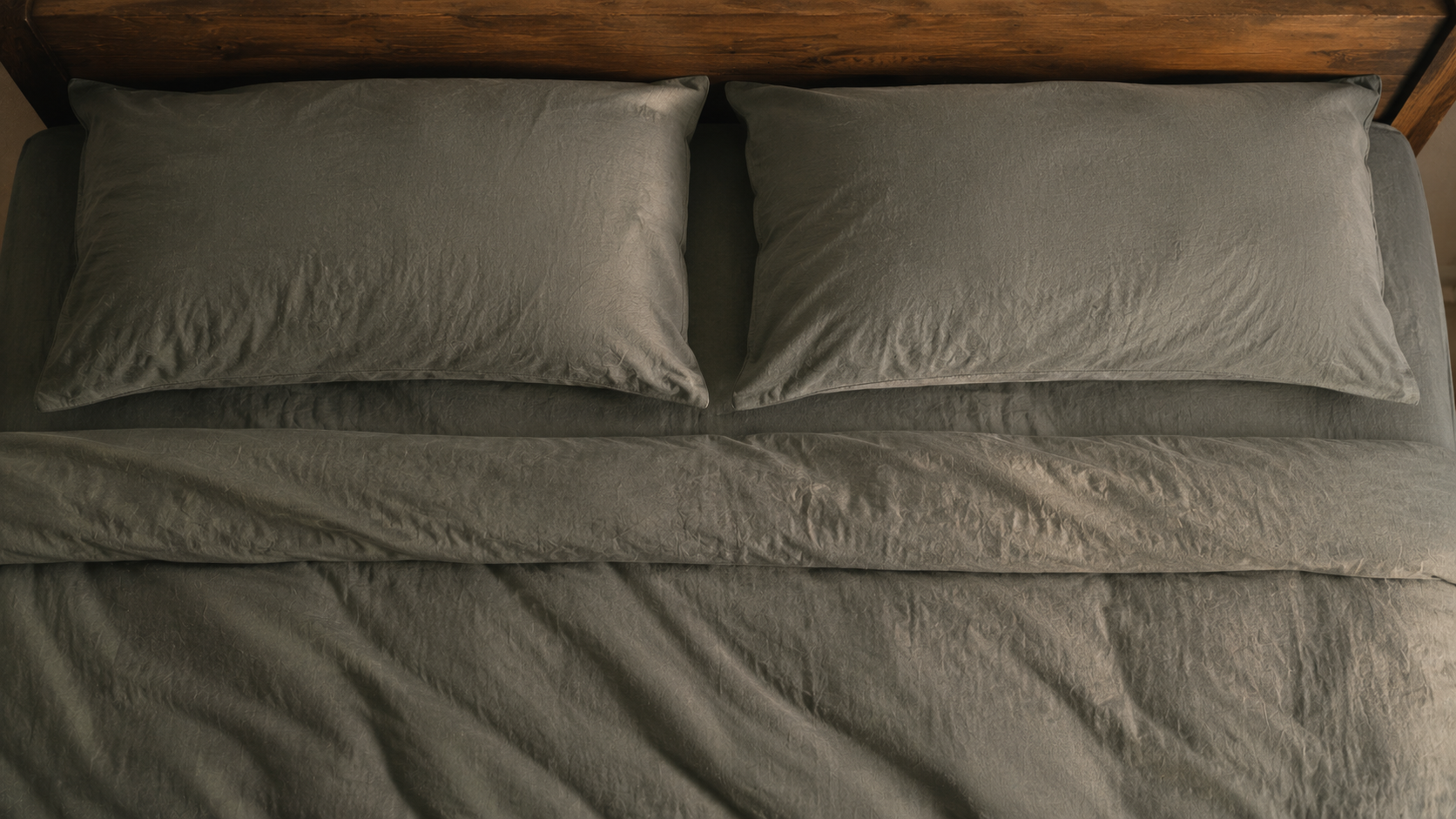Neatly made bed seen from directly above with two grey-green pillows side by side in soft dawn light