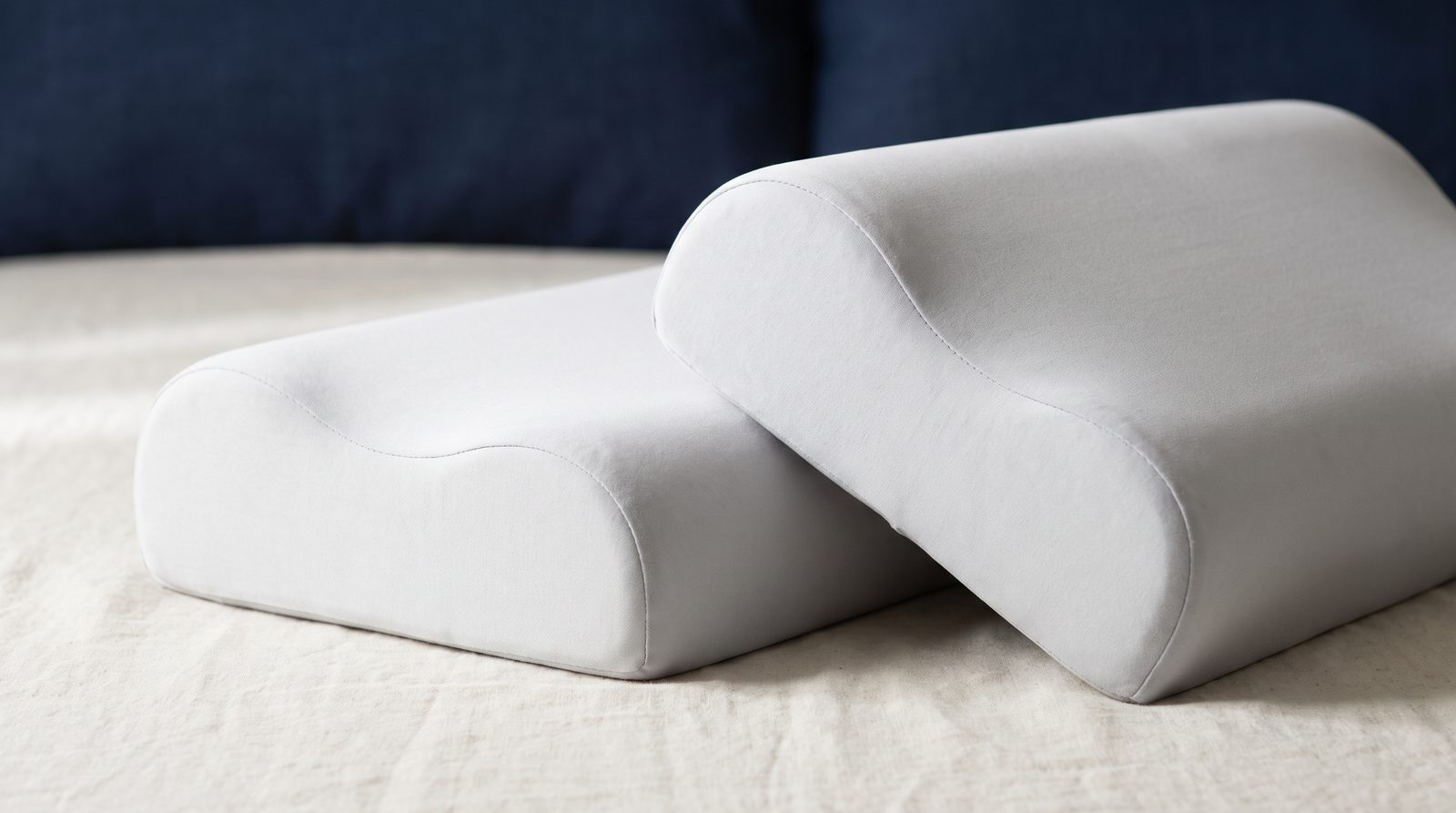 Two unbranded contoured memory foam neck pillows side by side, photographed in profile so the neck curves are visible