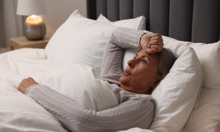 Woman in her fifties lying awake in bed at night with her hand on her forehead
