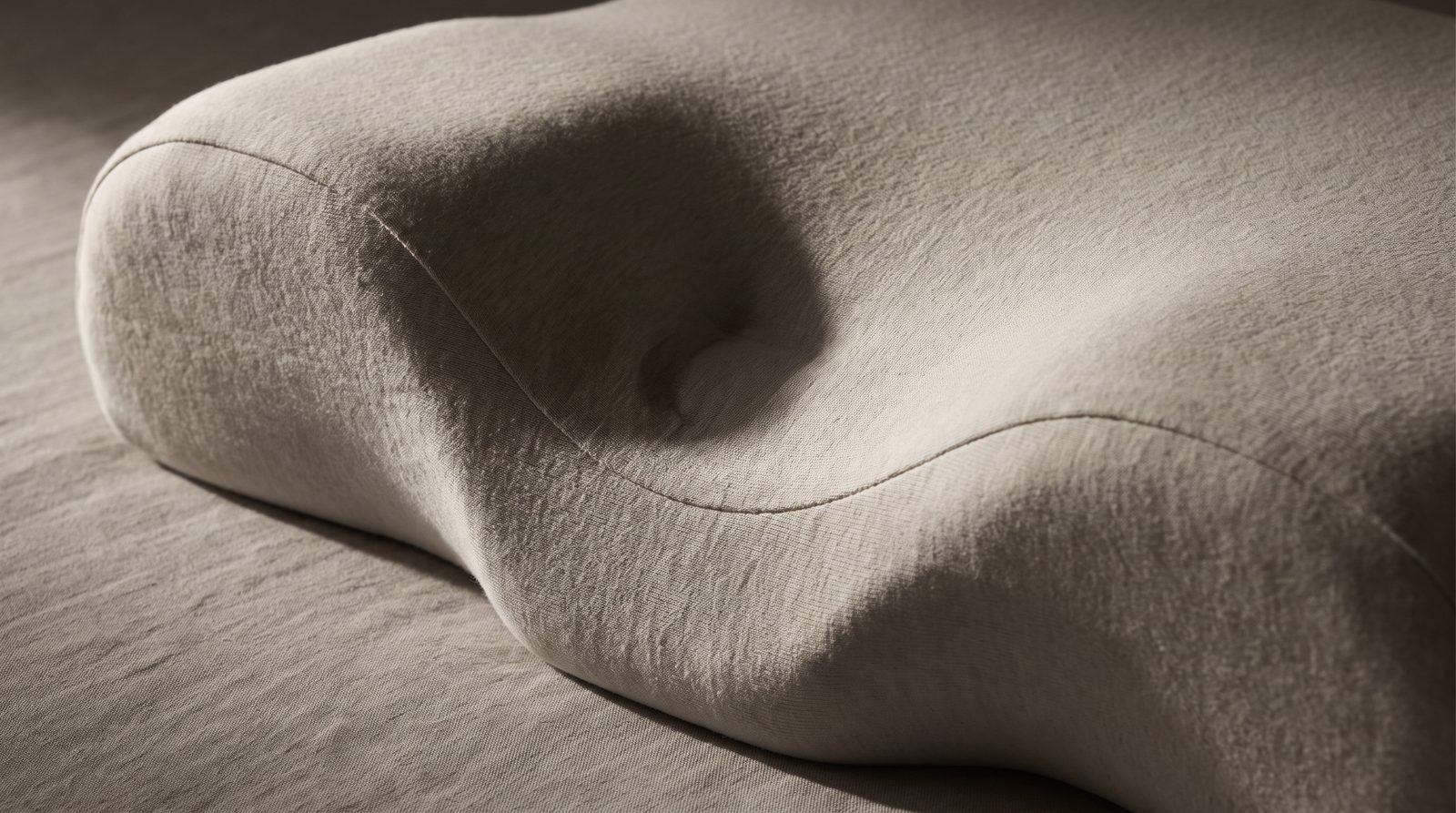 Macro view of a memory-foam cervical pillow in raking light, showing the raised neck roll and recessed centre