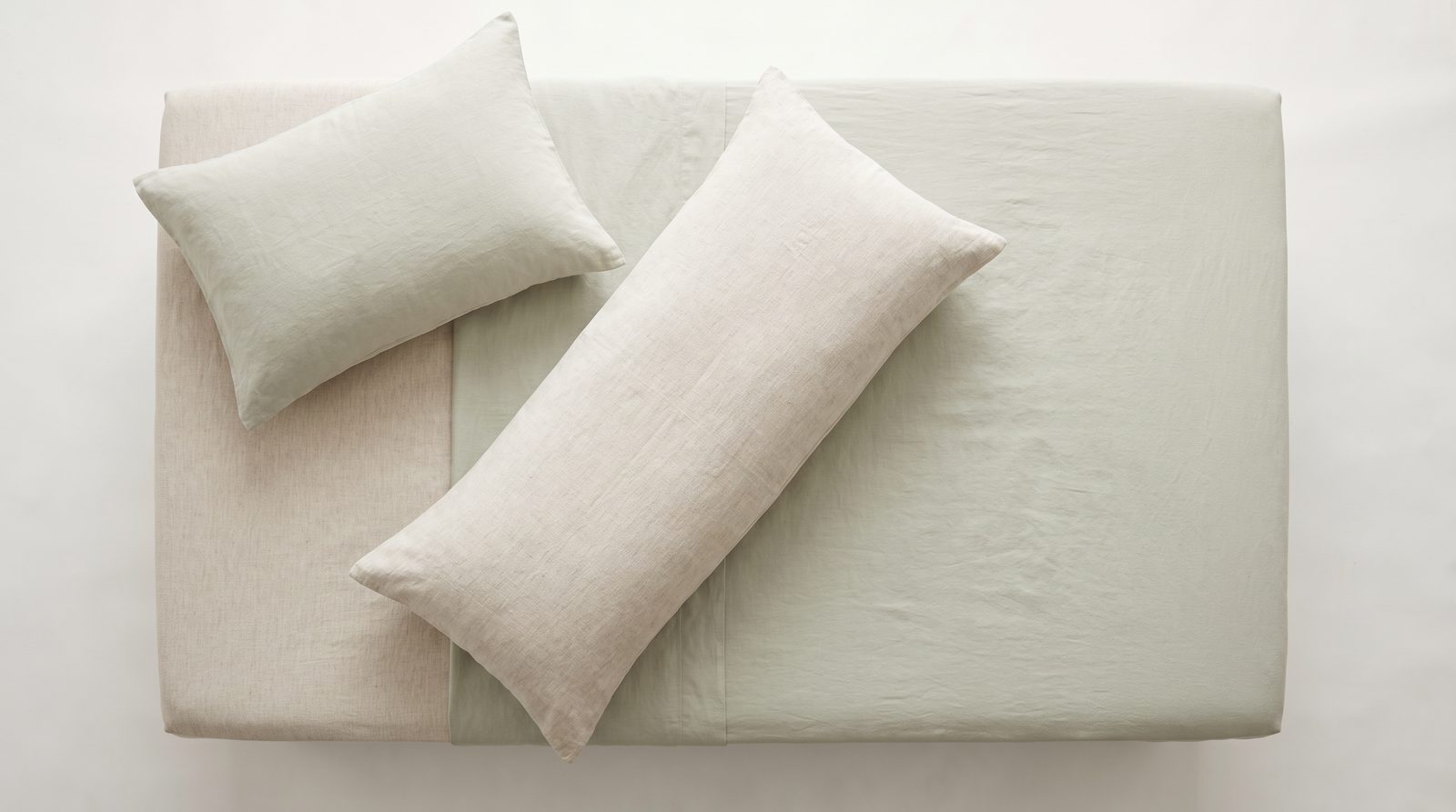 Overhead view of a bed made up for side sleeping, with a head pillow and a second firm pillow placed where it would sit between the knees